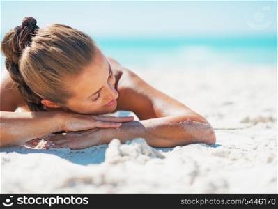 Happy young woman in swimsuit relaxing while laying on sandy beach