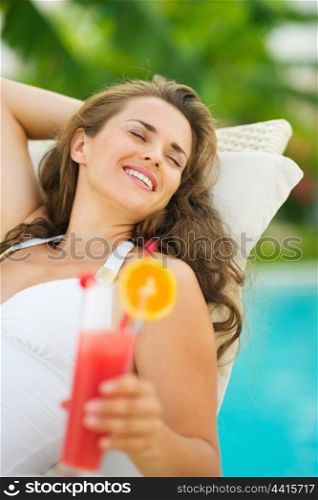 Happy young woman in swimsuit relaxing with cocktail on chaise-longue
