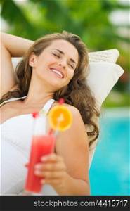 Happy young woman in swimsuit relaxing with cocktail on chaise-longue