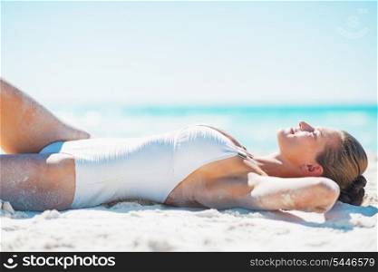 Happy young woman in swimsuit tanning on beach