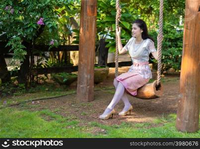 happy young woman in Thai traditional dress relaxing on a wooden swing