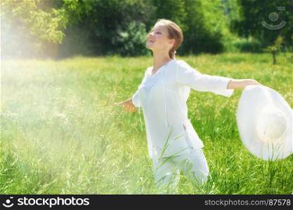 Happy Young Woman in White Clothes Running with a White Hat at the Green Meadow.