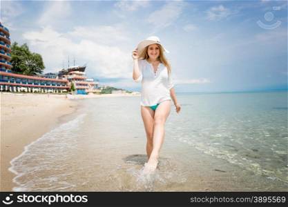 Happy young woman in white hat walking on the seashore