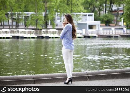Happy young woman in white pants and a blue shirt walking in the summer park