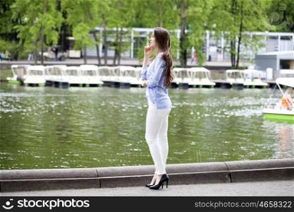 Happy young woman in white pants and a blue shirt walking in the summer park