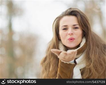 Happy young woman in winter jacket blowing kiss outdoors