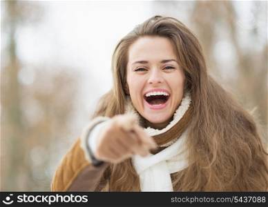 Happy young woman in winter outdoors pointing in camera