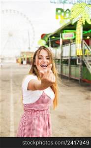 happy young woman inviting someone with one hand amusement park