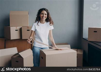 Happy young woman is packing boxes with duct tape. Attractive lady is wrapping cardboard boxes with packing tape. Moving service worker preparing cargo for shipping and storage.. Happy young woman is packing boxes with duct tape. Moving service worker preparing cargo.