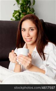 Happy young woman is relaxing on comfortable couch and drinking hot tea