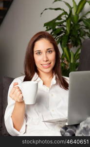 Happy young woman is relaxing on comfortable couch and using laptop at home.