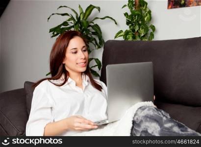 Happy young woman is relaxing on comfortable couch and using laptop at home.