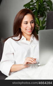 Happy young woman is relaxing on comfortable couch and using laptop at home.