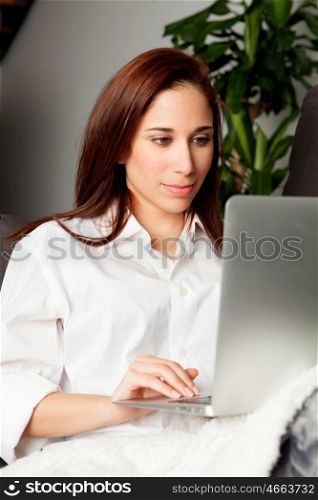 Happy young woman is relaxing on comfortable couch and using laptop at home. &#xA;