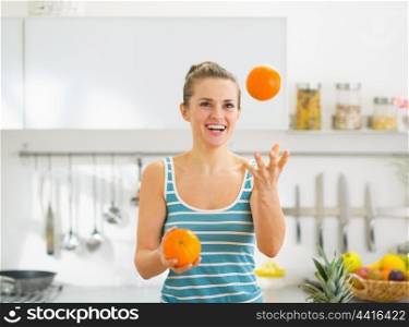 Happy young woman joggling with oranges in kitchen
