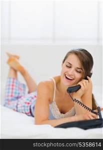 Happy young woman laying in bed and making phone call