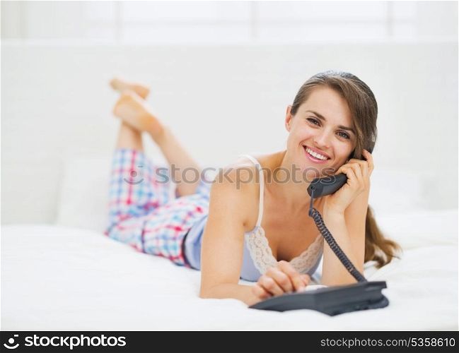 Happy young woman laying in bed and talking phone