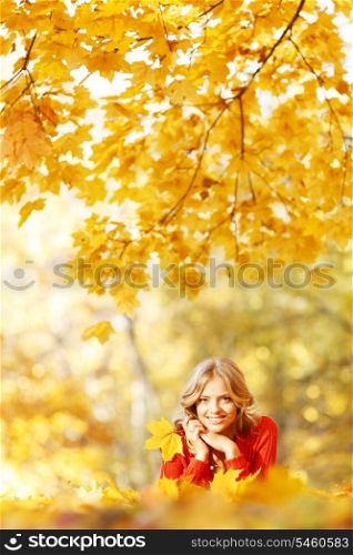 Happy young woman laying on autumn leaves in park