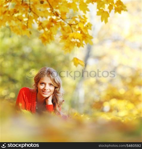 Happy young woman laying on autumn leaves in park