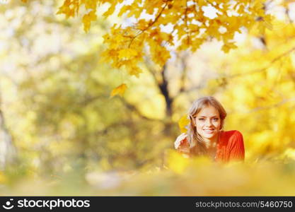 Happy young woman laying on autumn leaves in park