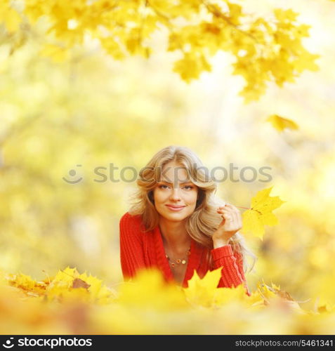 Happy young woman laying on autumn leaves in park