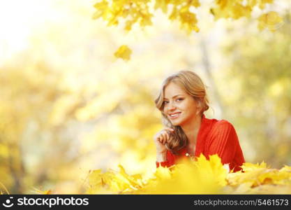 Happy young woman laying on autumn leaves in park