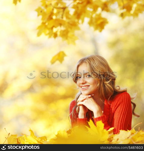 Happy young woman laying on autumn leaves in park