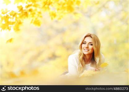 Happy young woman laying on autumn leaves in park. Woman laying on autumn leaves