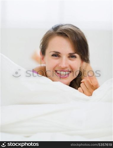 Happy young woman laying on bed and beckoning with finger