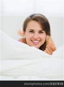 Happy young woman laying on bed and beckoning with finger