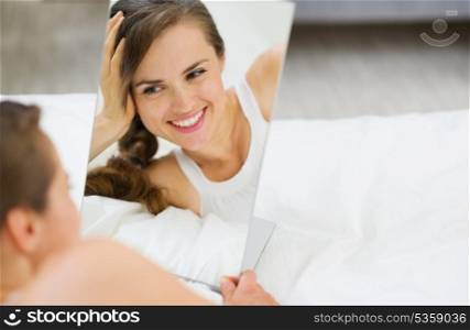 Happy young woman laying on bed and looking on mirror