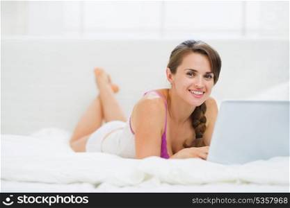 Happy young woman laying on bed and surfing internet