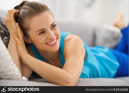 Happy young woman laying on couch in living room and looking on copy space