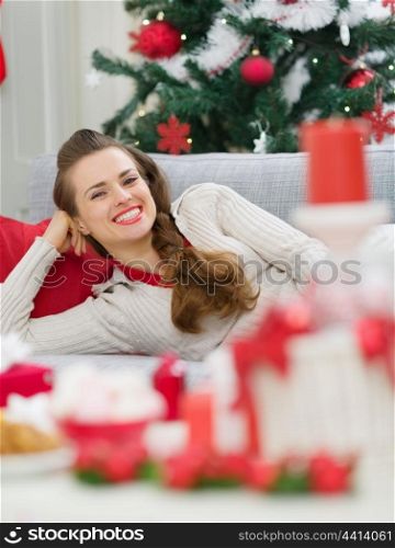 Happy young woman laying on couch near Christmas tree