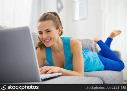 Happy young woman laying on divan and using laptop