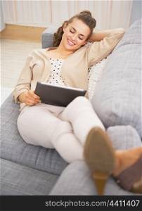 Happy young woman laying on divan and using tablet pc
