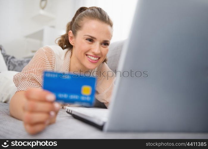 Happy young woman laying on divan with laptop and credit card