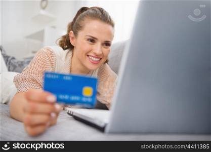 Happy young woman laying on divan with laptop and credit card