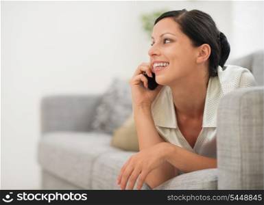 Happy young woman laying on sofa and speaking cell phone