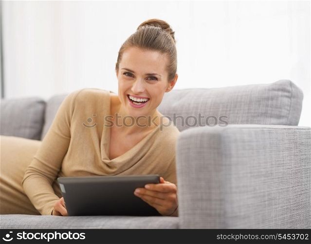 Happy young woman laying on sofa with tablet pc