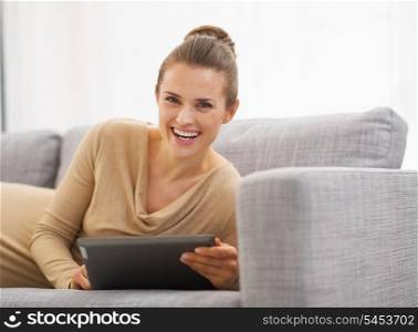 Happy young woman laying on sofa with tablet pc