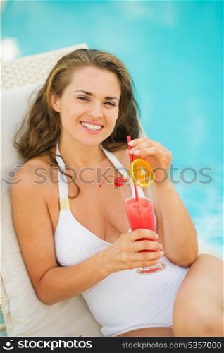 Happy young woman laying on sunbed enjoying cocktail at poolside