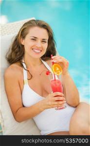 Happy young woman laying on sunbed enjoying cocktail at poolside