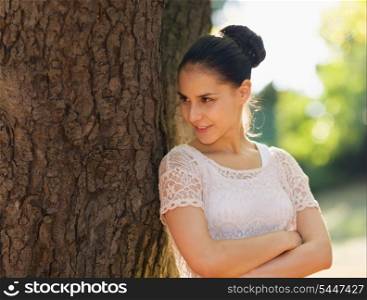 Happy young woman lean against tree and looking on copy space