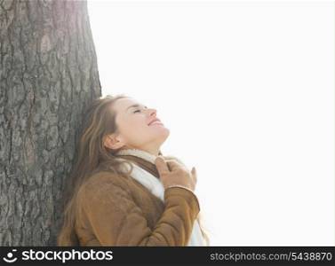 Happy young woman leaning against tree in winter park