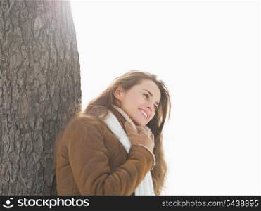Happy young woman leaning against tree in winter park