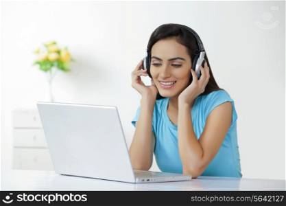 Happy young woman listening to headphones in front of laptop at home