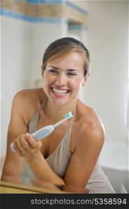 Happy young woman looking in mirror after brushing teeth with electric toothbrush