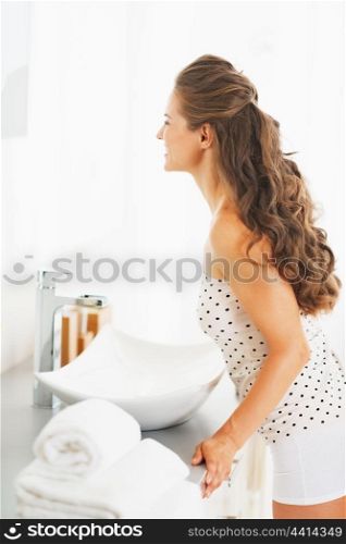 Happy young woman looking in mirror in bathroom