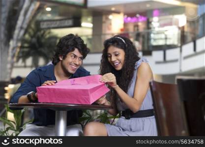 Happy young woman looking inside bag with man smiling